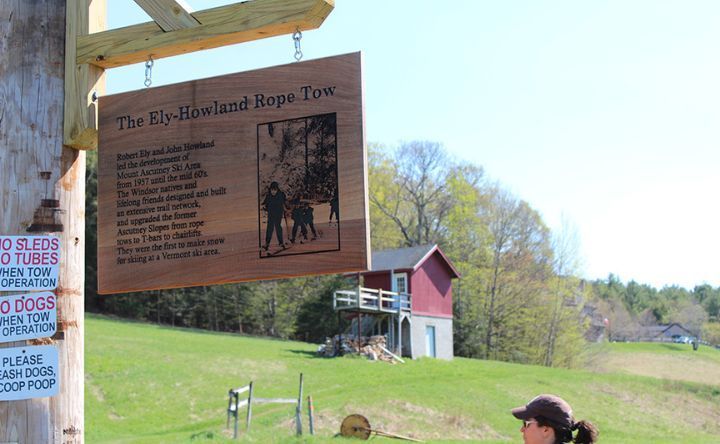 A woman is standing in a field next to a sign that says the city highland rope tow.