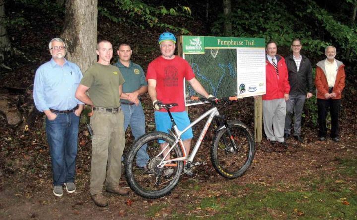 A group of people standing next to a bicycle and a sign that says preserve trail.