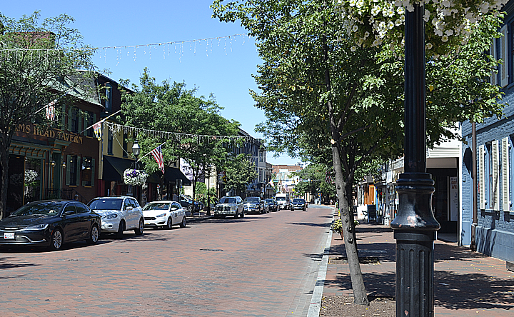 A row of cars are parked on a brick street in a small town.