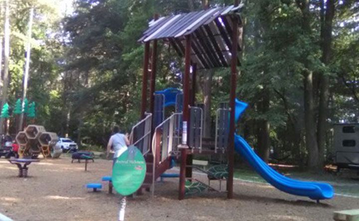 A man is standing in front of a playground with a blue slide.