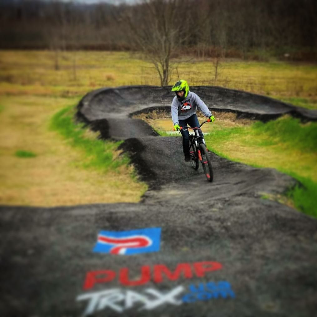 A person is riding a bike on a track that says pump trax on it