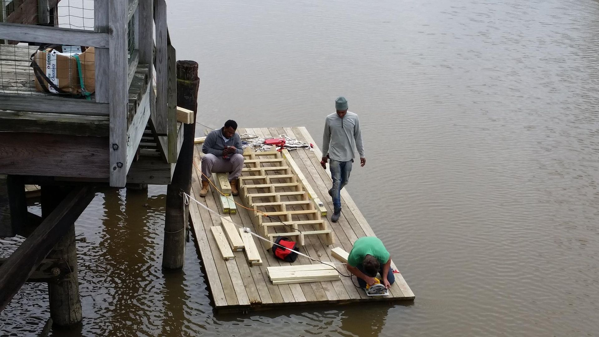 Two men are working on a wooden raft in the water
