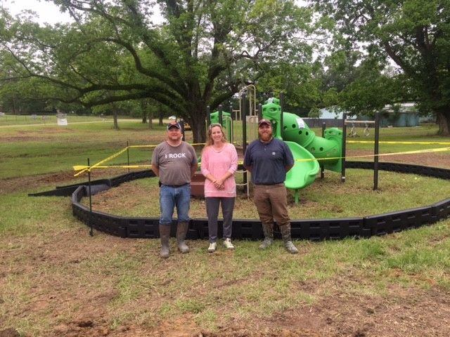 Three people are standing in front of a playground in a park.
