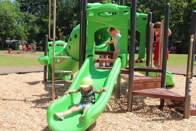 A little girl is sitting on a green slide at a playground.