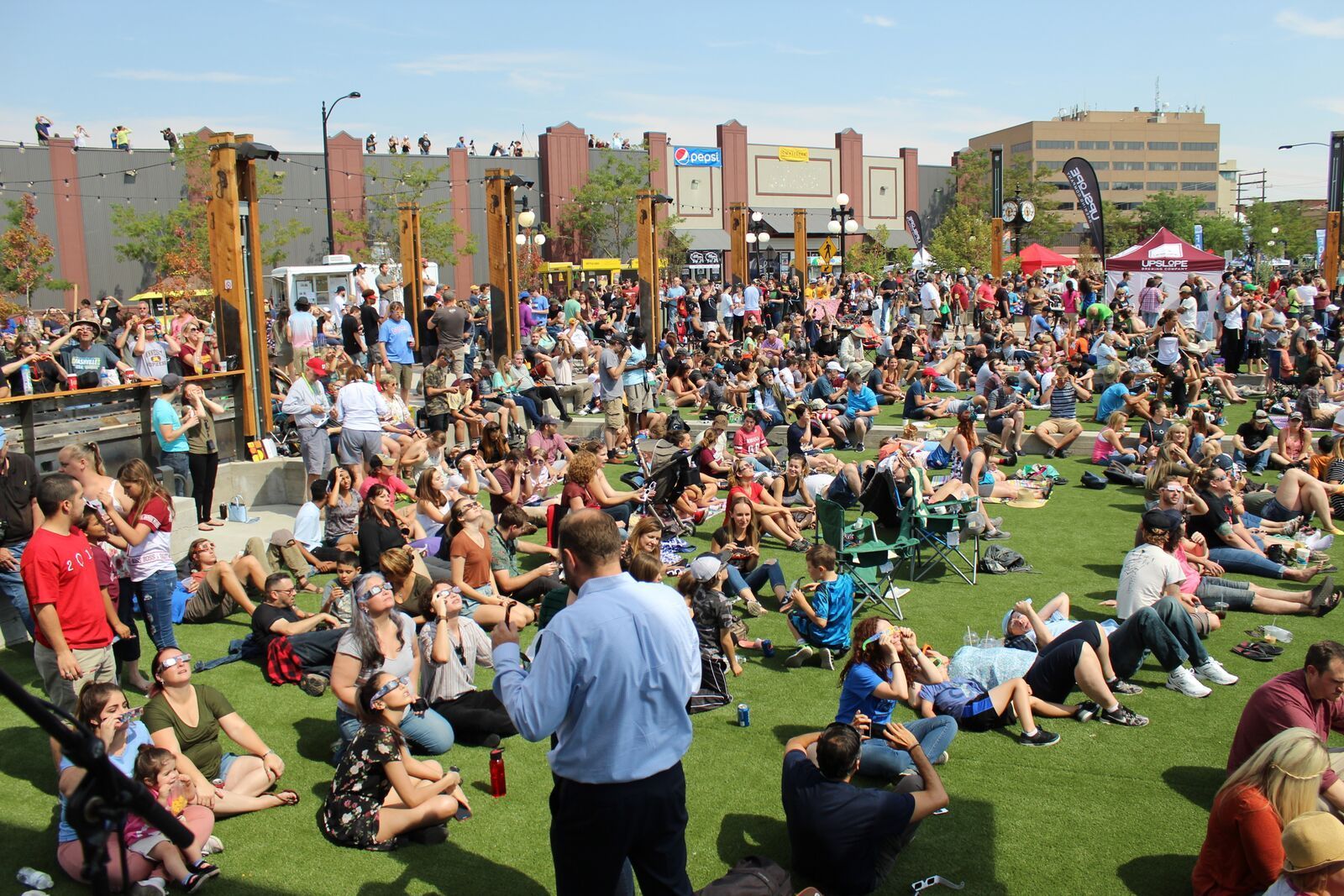 A man is standing in front of a crowd of people sitting on the grass.