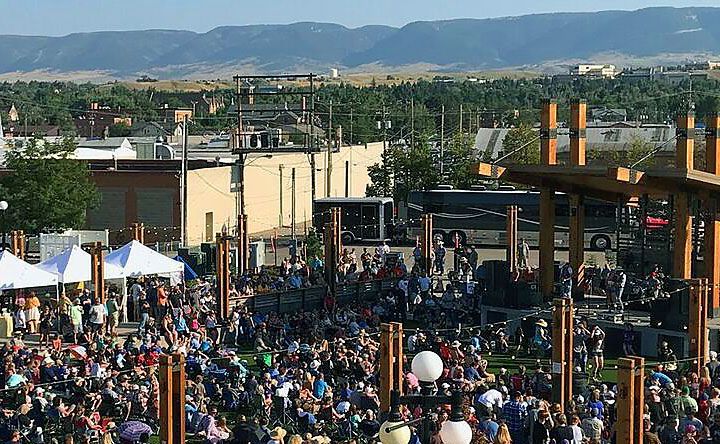 A large crowd of people are gathered in a park with mountains in the background.