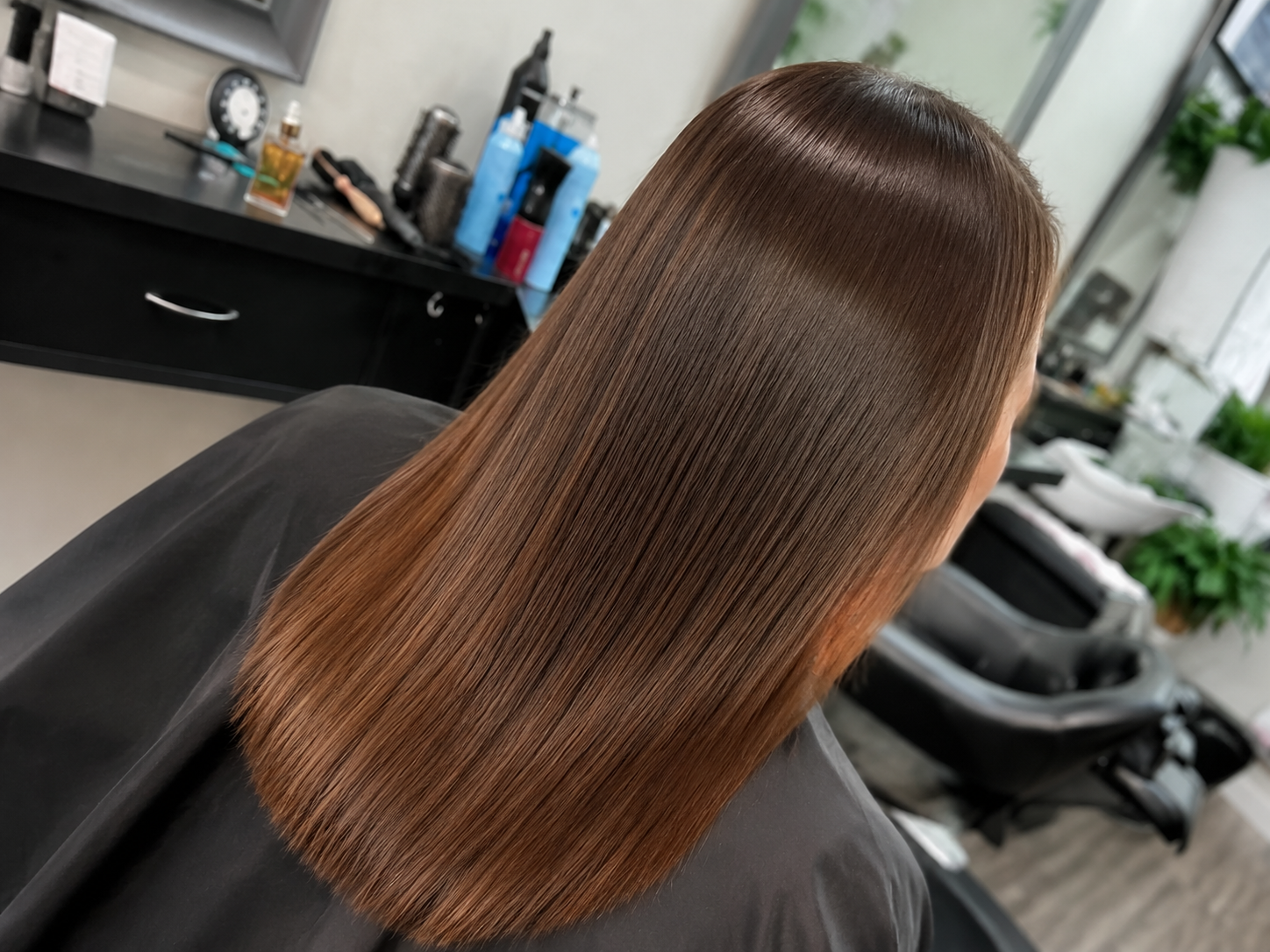 Glossy straight auburn hair styled in a salon chair, viewed from behind.