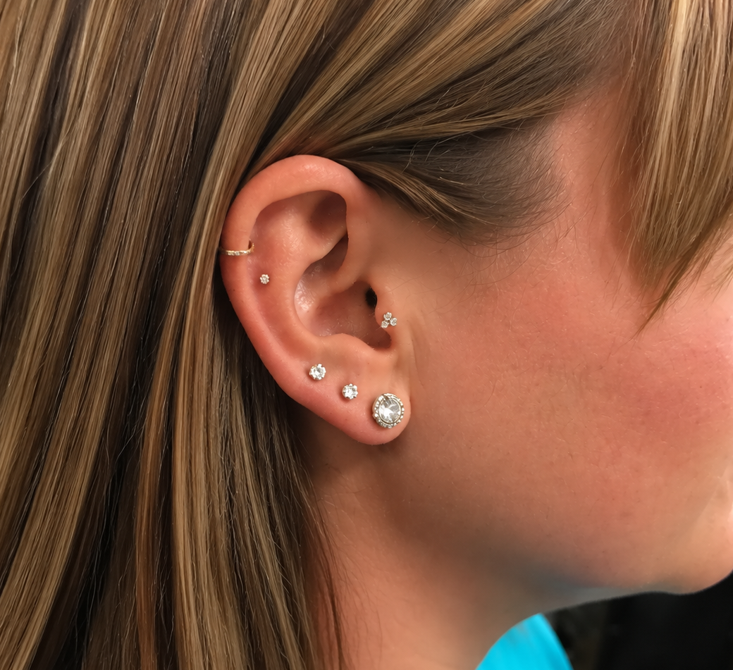 Close-up of an ear with multiple sparkling stud earrings and a small hoop, side profile against a plain background