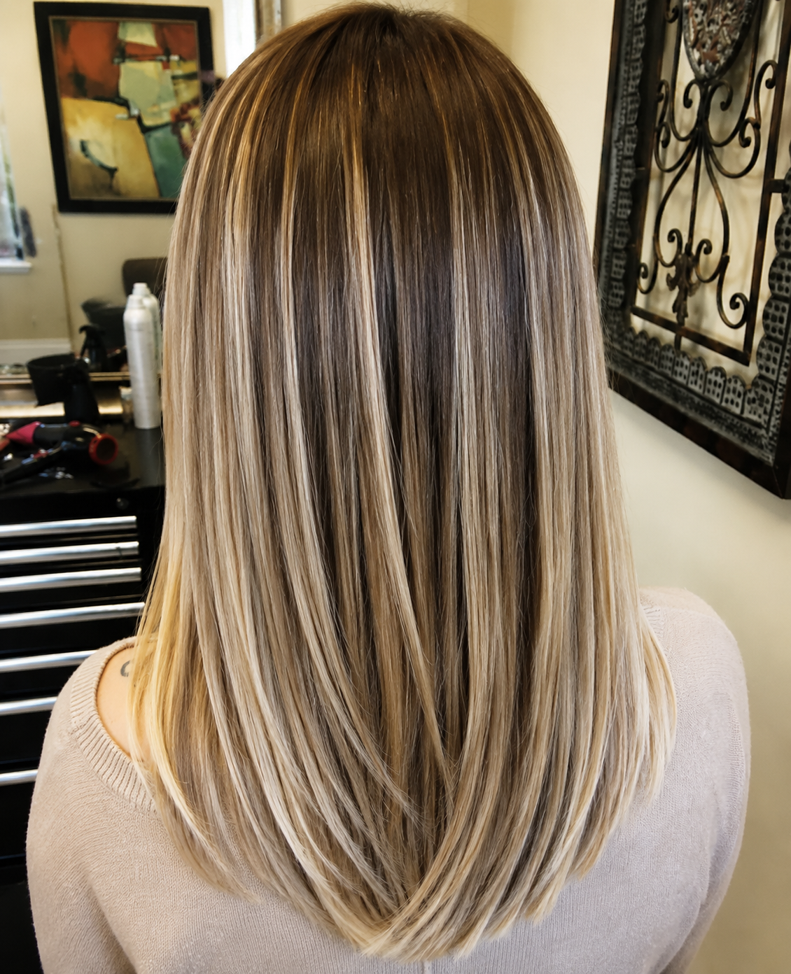 Blonde highlighted shoulder-length hair with smooth layers, shown from the back in a salon setting