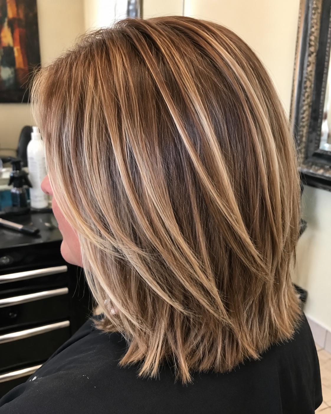 Layered brown bob hairstyle with blonde highlights, shown from the side in a salon setting