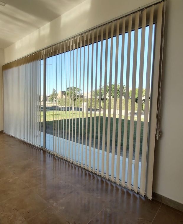 En un luminoso y moderno salón con suelo de madera y un sofá gris claro, cuelgan cortinas color crema 