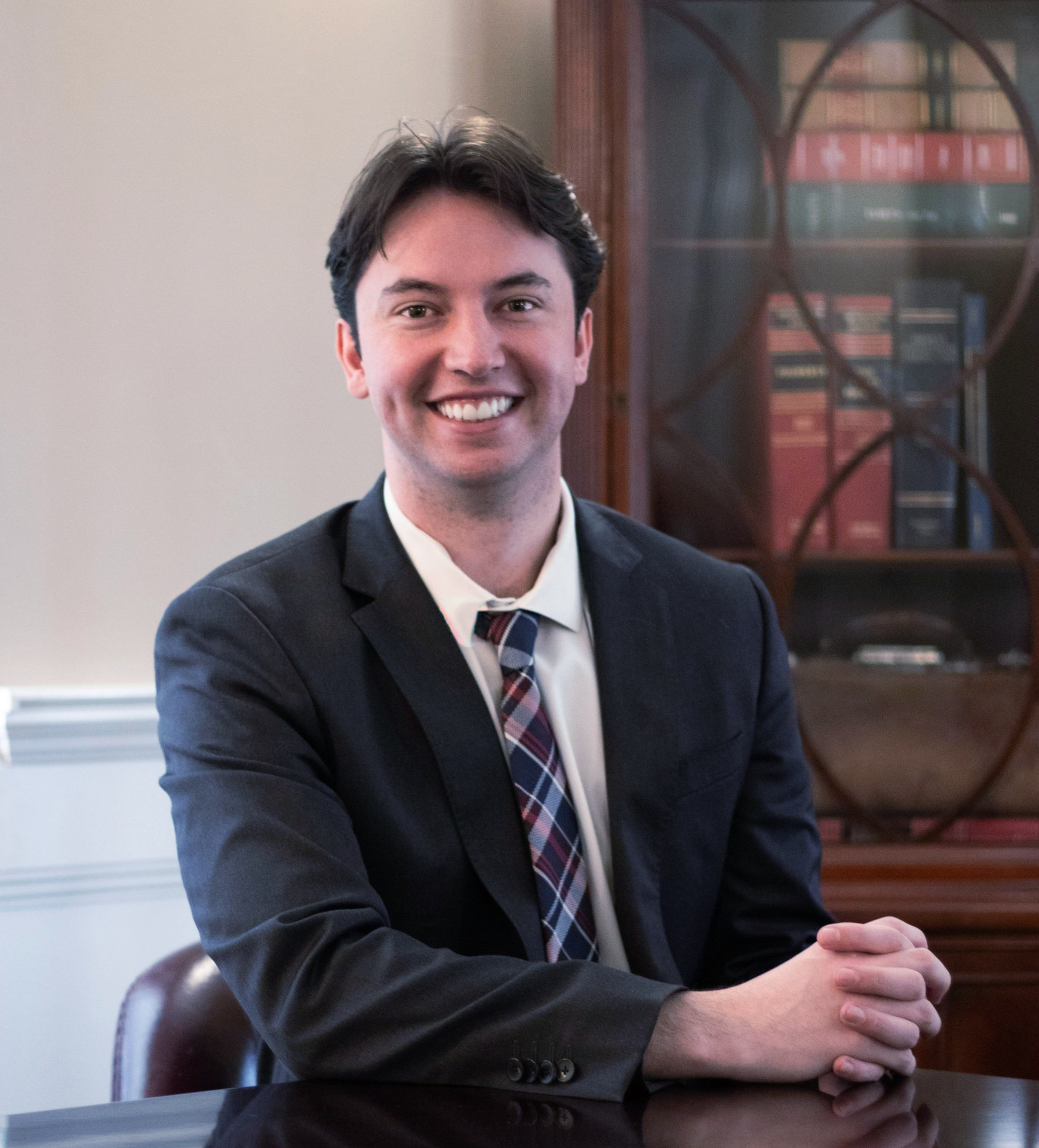 Thomas Doran in a suit and tie is sitting in front of a bookcase