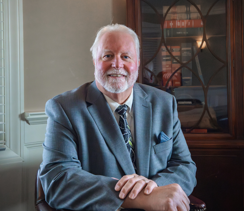 Thomas Doran in a suit and tie is sitting in front of a bookcase