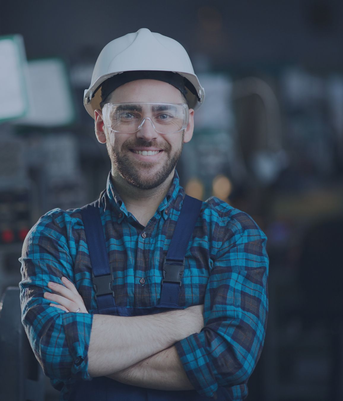a man wearing a hard hat and goggles is standing with his arms crossed in a factory representing Workers Compensation