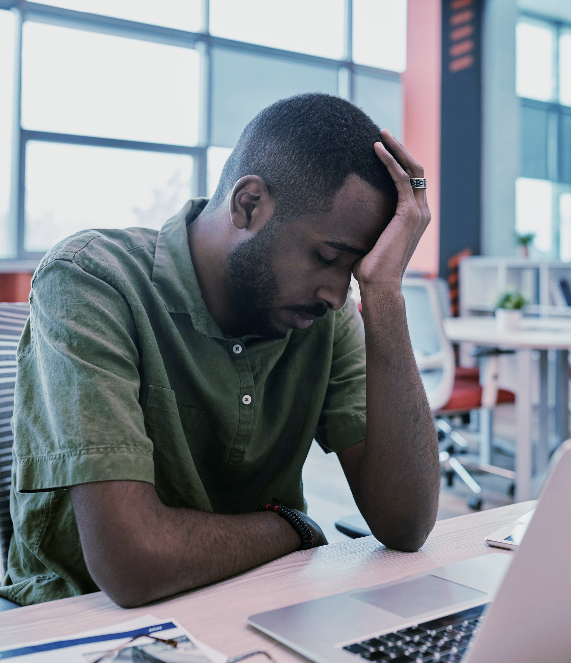 Man sitting at a table, head in hand, looking down at a laptop in a bright office researching legal options