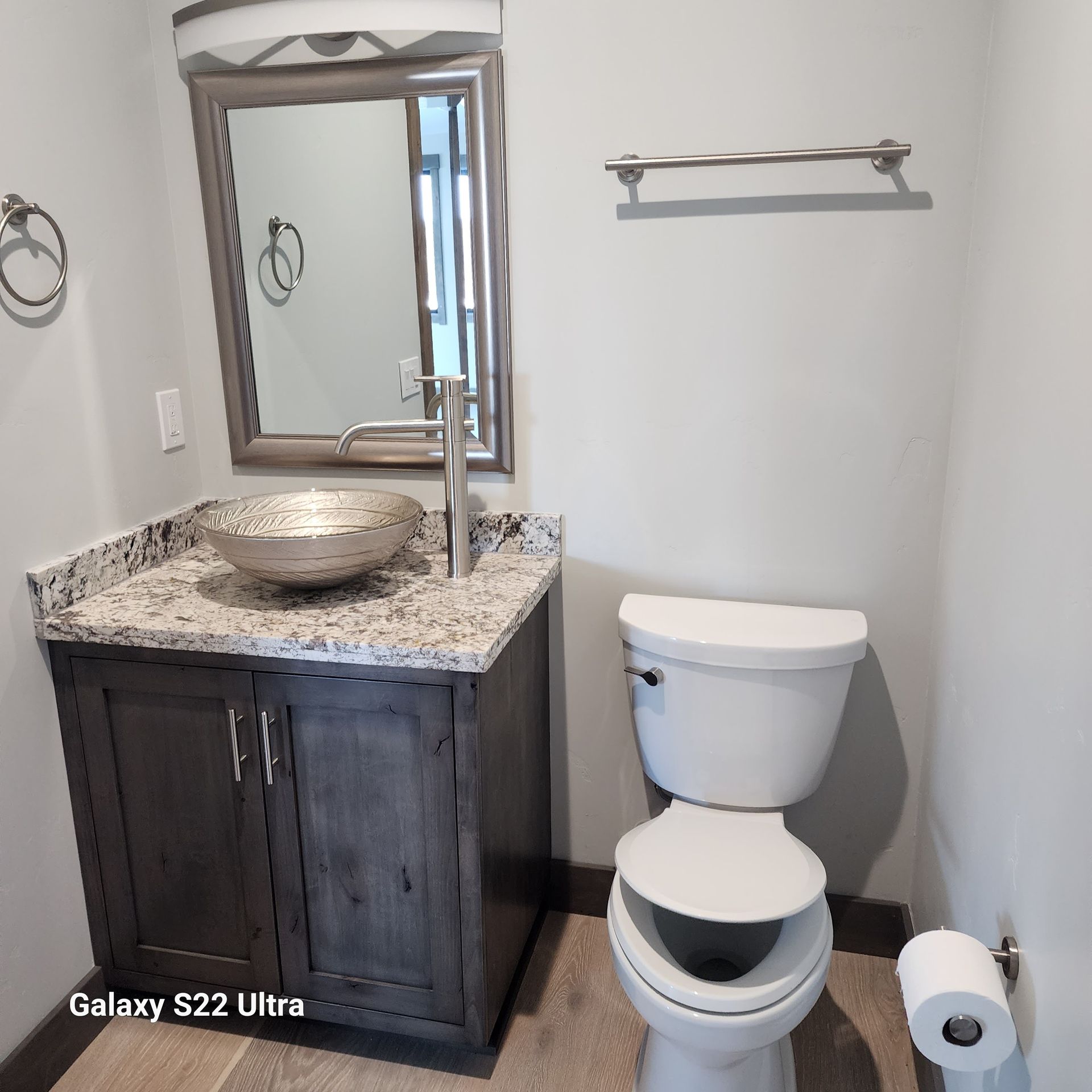 Small bathroom with dark vanity, vessel sink, mirror, toilet, towel rack, and toilet paper holder.