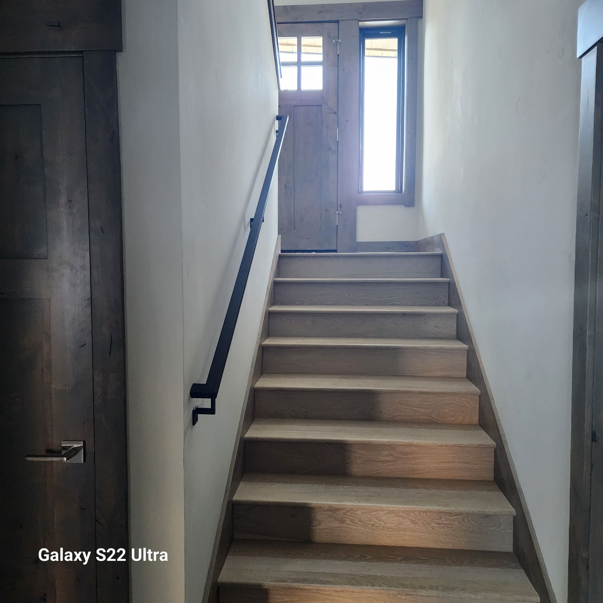 Narrow indoor staircase with beige steps, dark handrail, and a small window at the top.