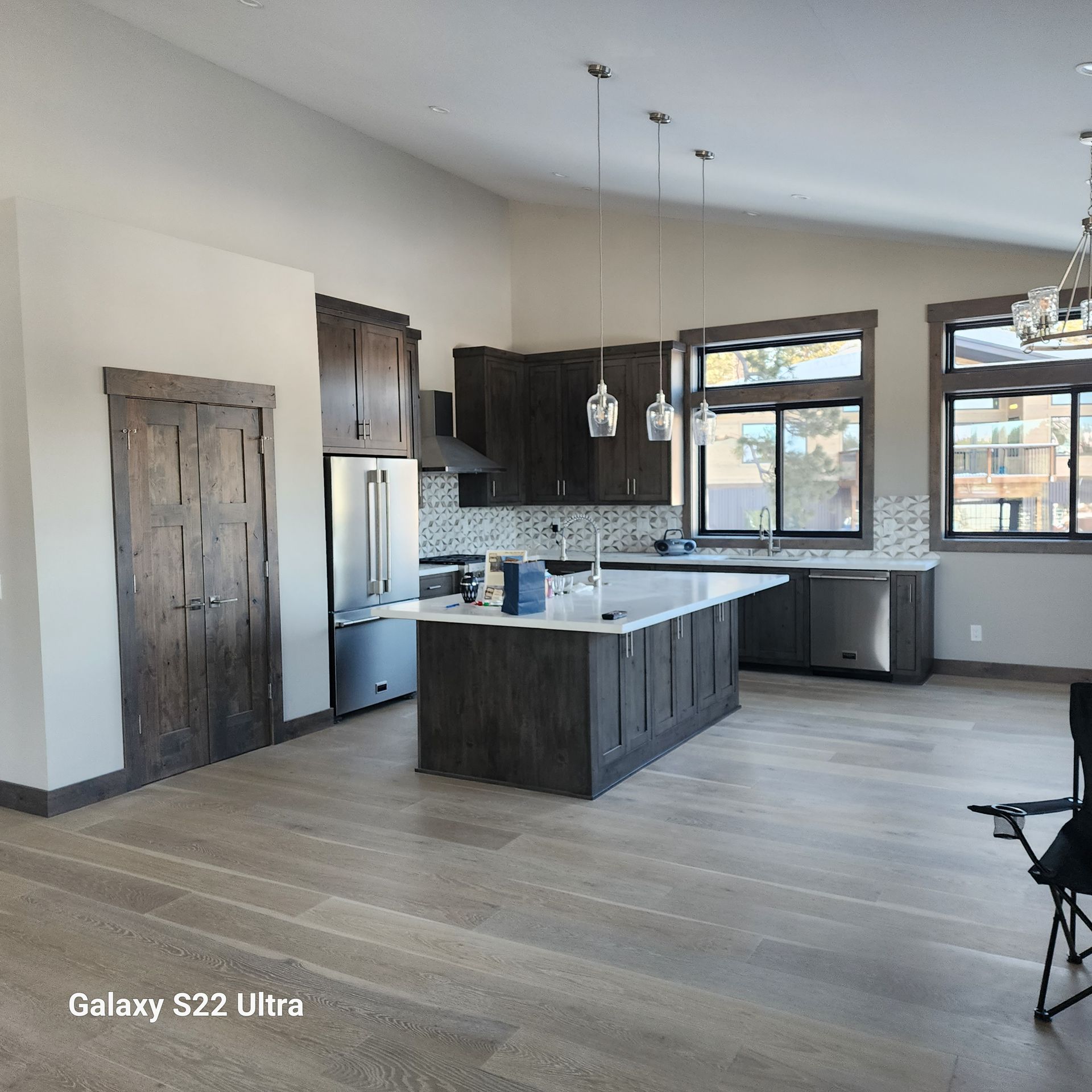 Modern kitchen with dark cabinets, white island, stainless fridge, and large windows in an open room