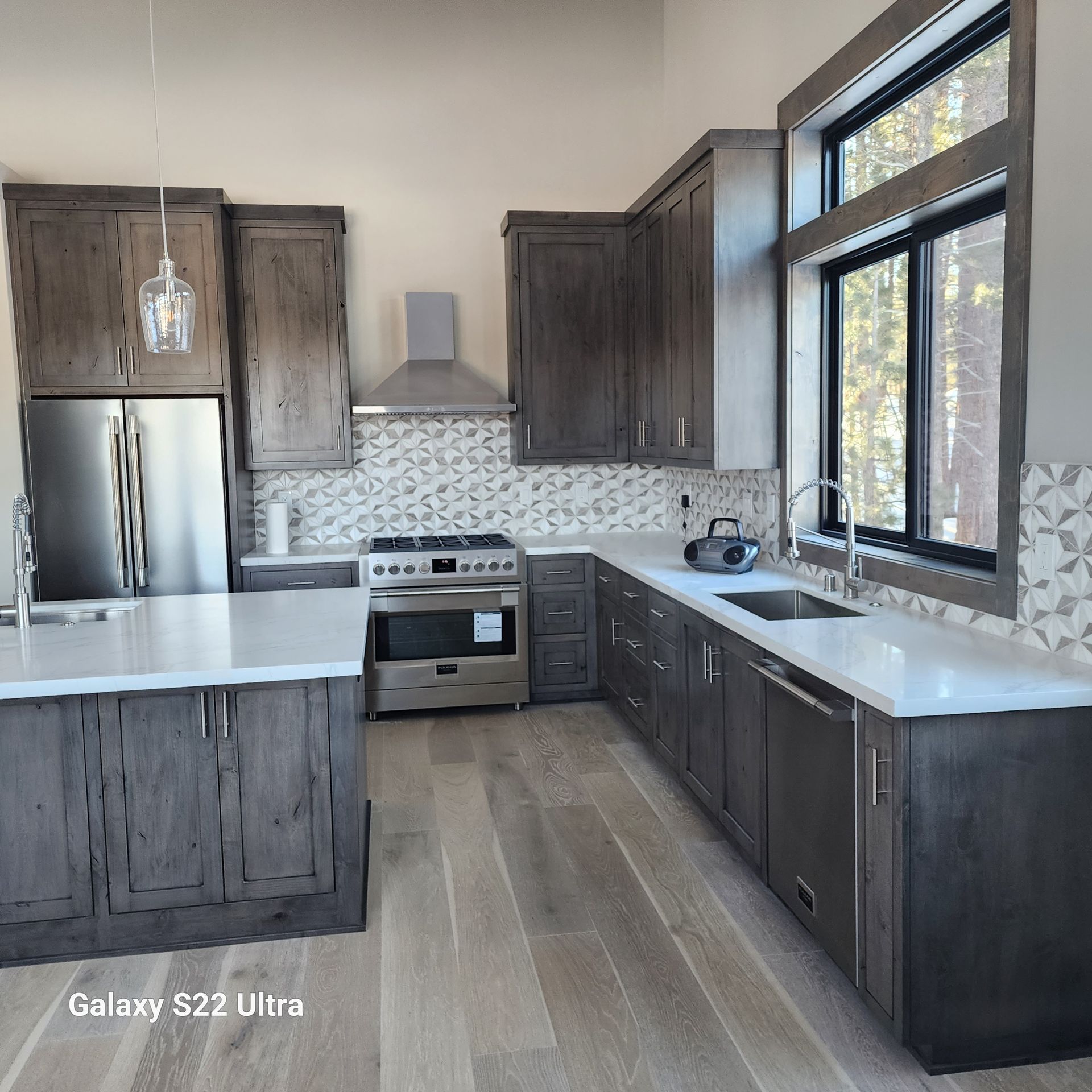 Modern kitchen with dark wood cabinets, white countertops, stainless appliances, and large windows