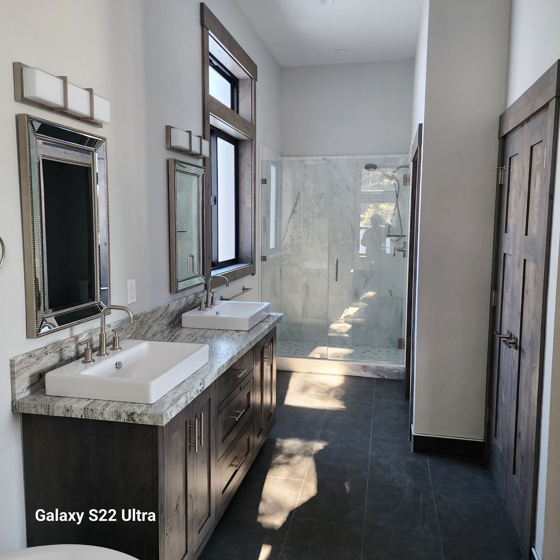 Modern bathroom with double vanity, large mirror, dark floor, and a glass shower at the back