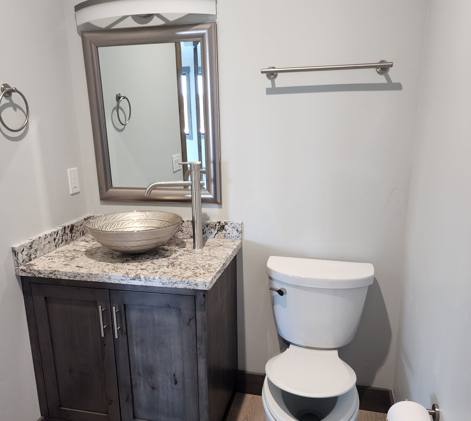 Small bathroom with rustic vanity, vessel sink, mirror, wall shelf, and toilet.