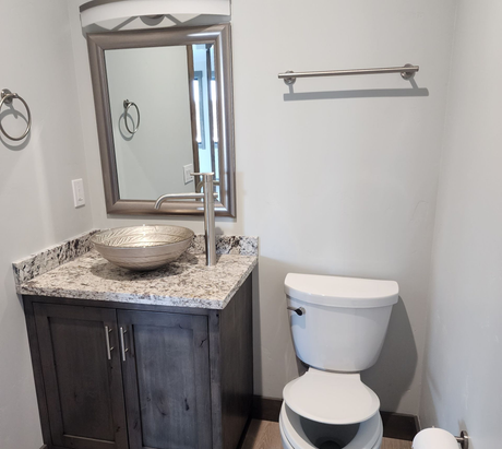 Modern bathroom with dark vanity, vessel sink, mirror, toilet, and towel rack on white walls