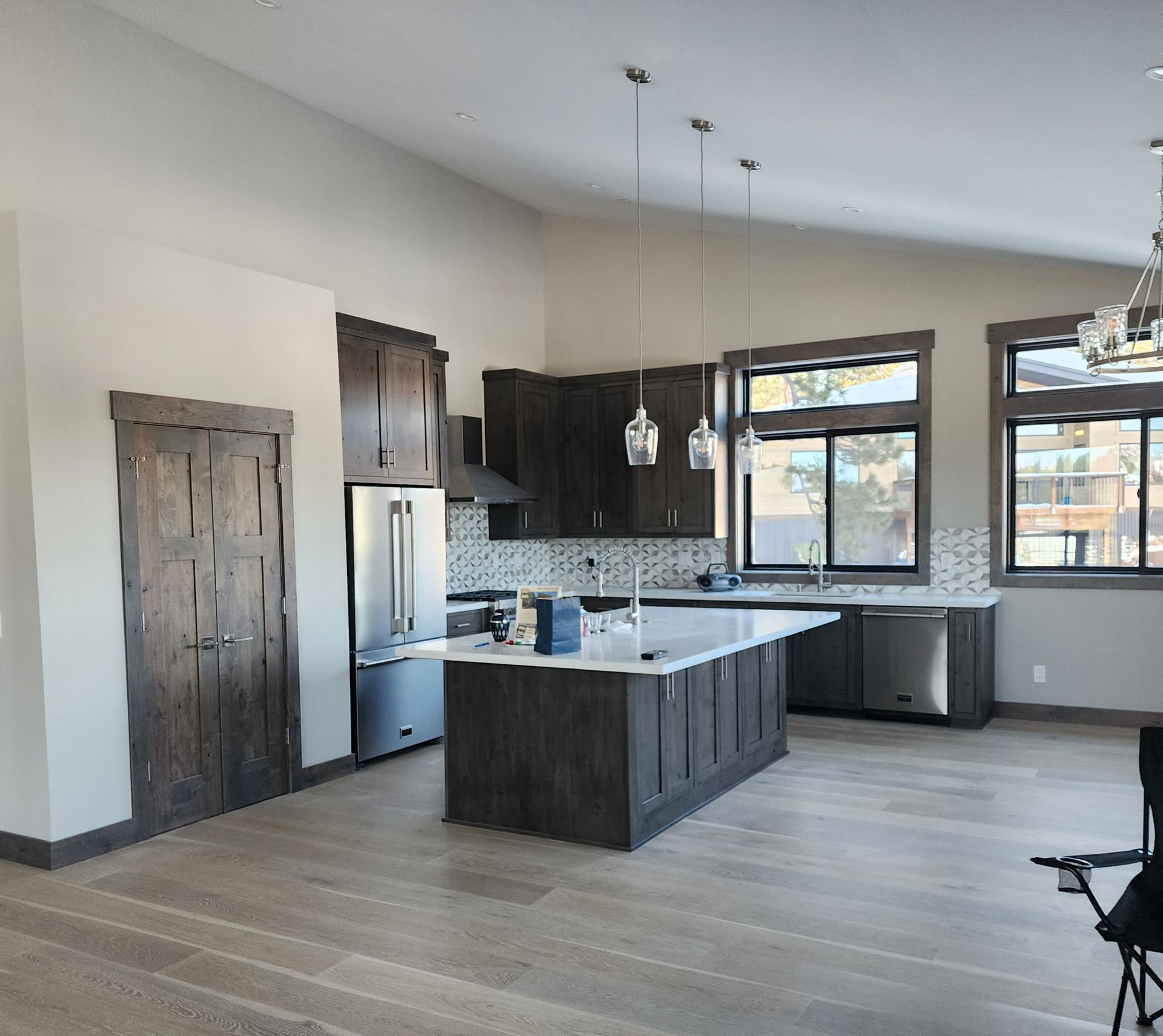 Modern open-concept kitchen with dark cabinets, granite island, stainless fridge, and large windows