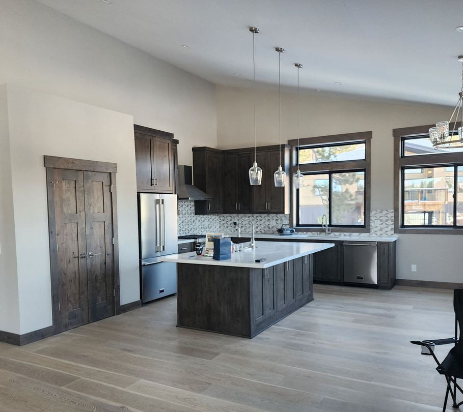 Modern open-concept kitchen with dark cabinets, granite island, stainless fridge, and large windows