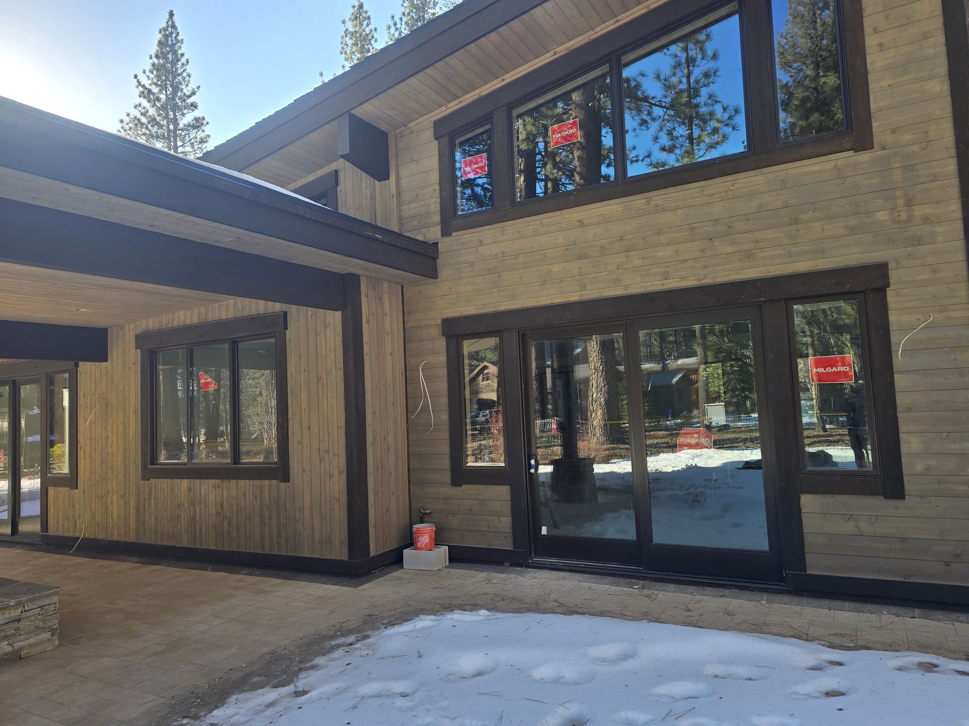 Modern beige house exterior with large windows, black trim, and snow on the ground