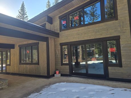 Modern beige house exterior with large windows, black trim, and snow on the ground