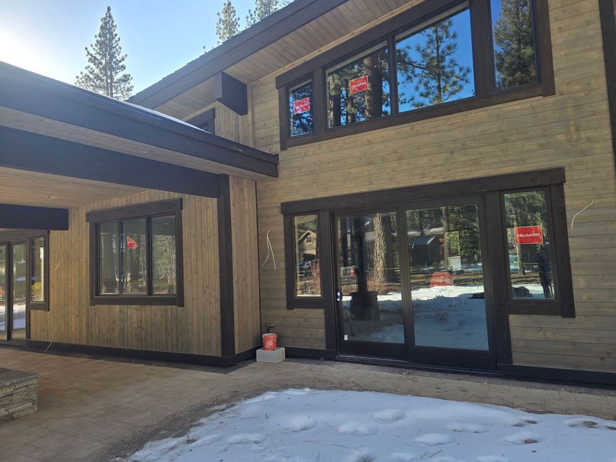 Modern beige house exterior with large windows, black trim, and snow on the ground