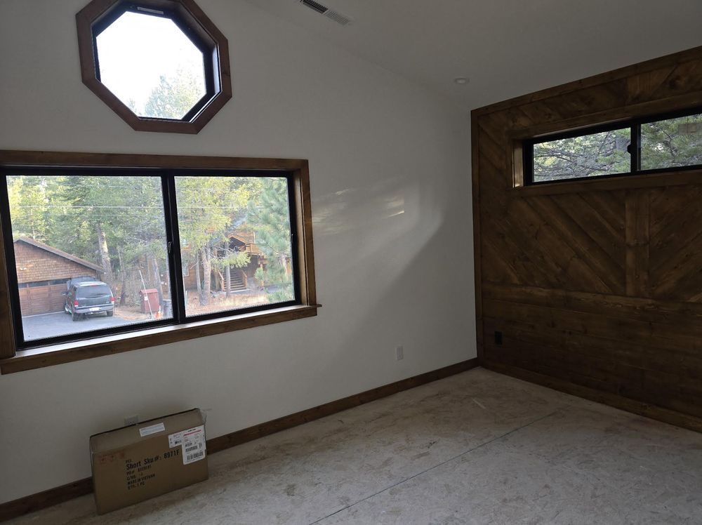 Empty room with wood-paneled wall, large windows, and a cardboard box on the floor.
