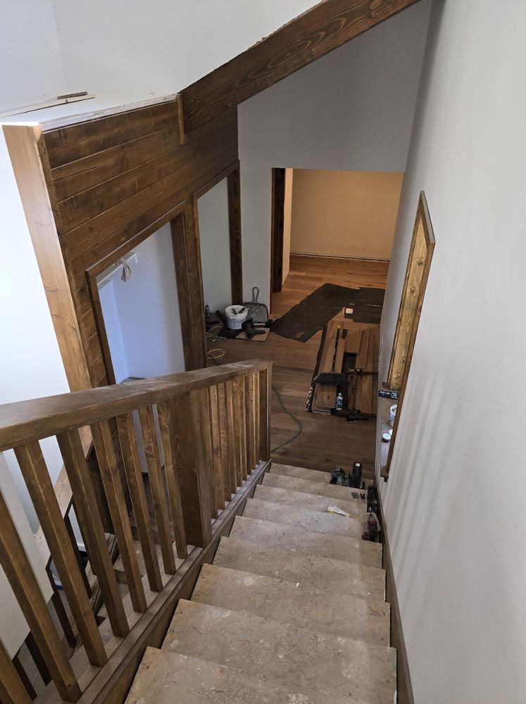 Staircase descending into a dim hallway with wooden railings and a rug at the bottom