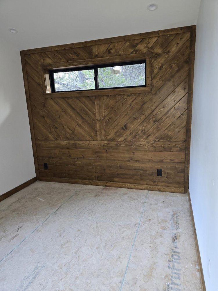 Empty room with wood-paneled accent wall, narrow window, and unfinished floor.