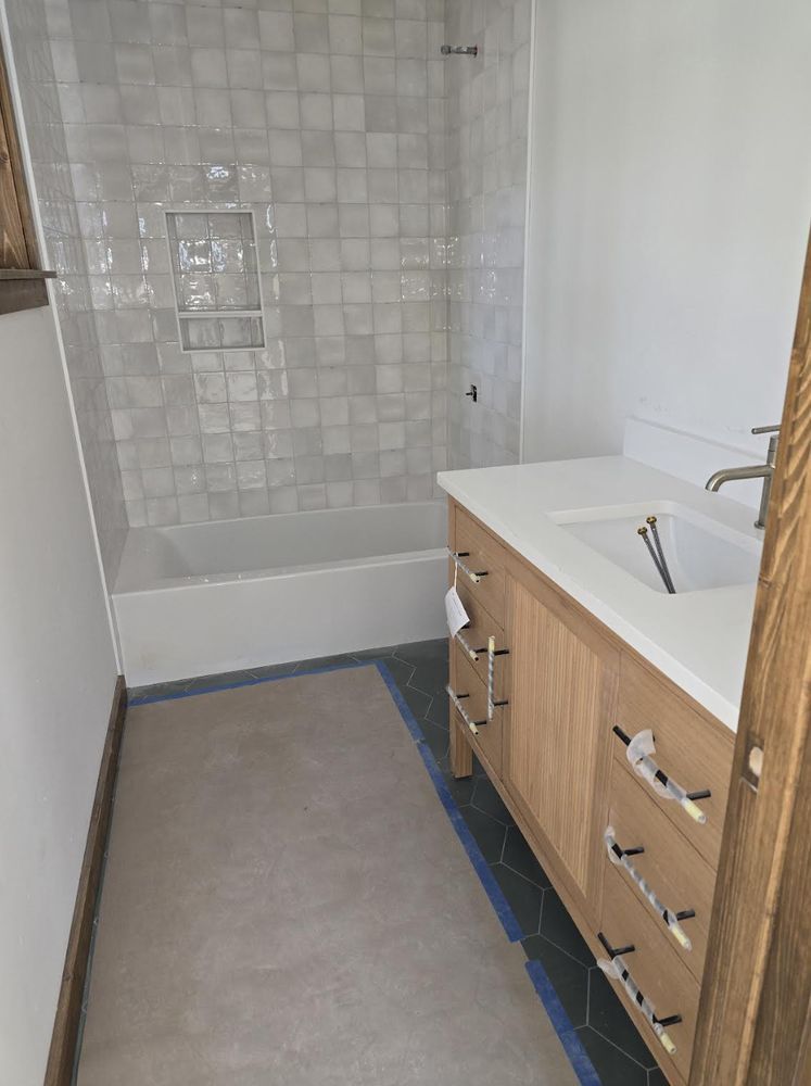 Modern bathroom with tub, white tile shower wall, gray floor, and wood vanity with sink