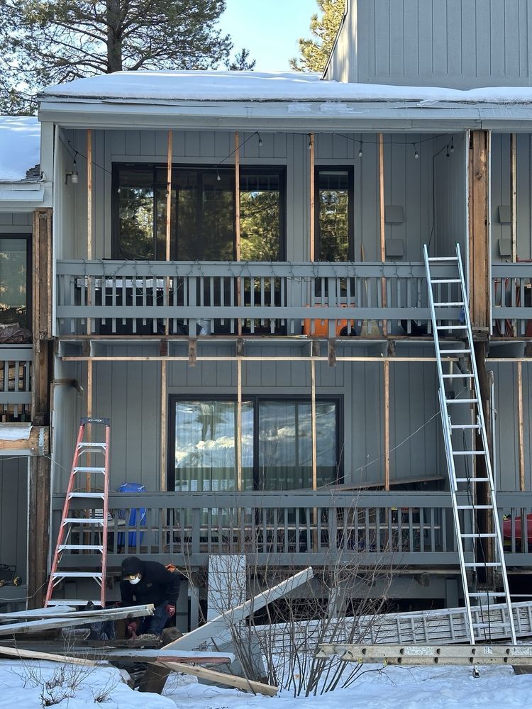 Two-story house exterior with porches, ladders, and snow on the ground during renovation