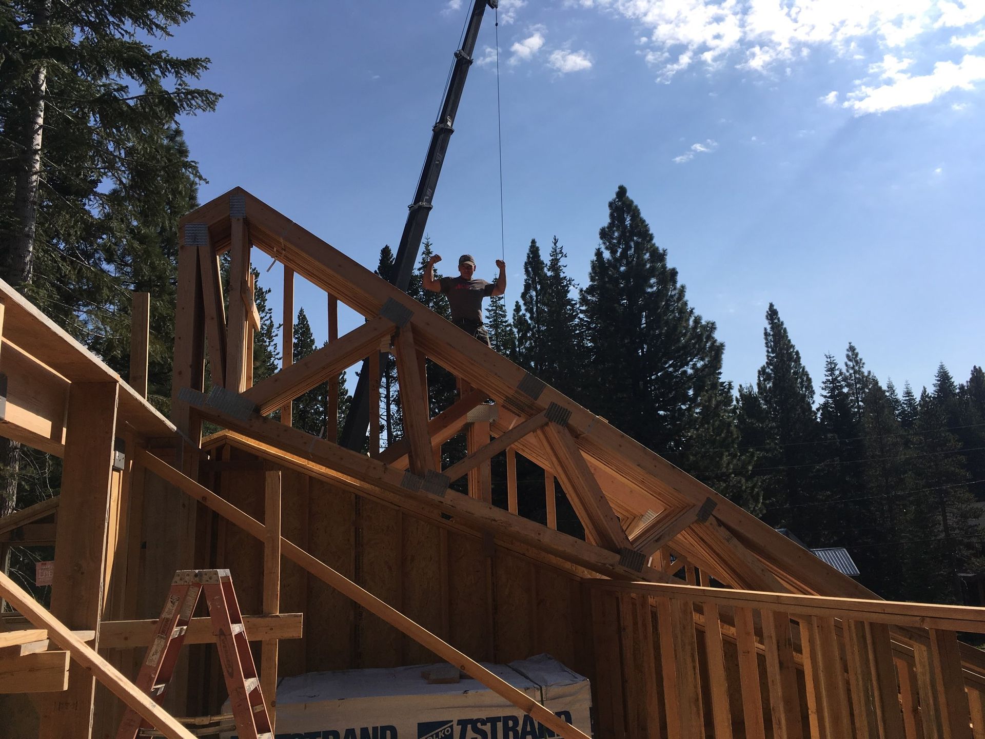 Workers using a crane to lift roof trusses onto a wooden house frame under construction