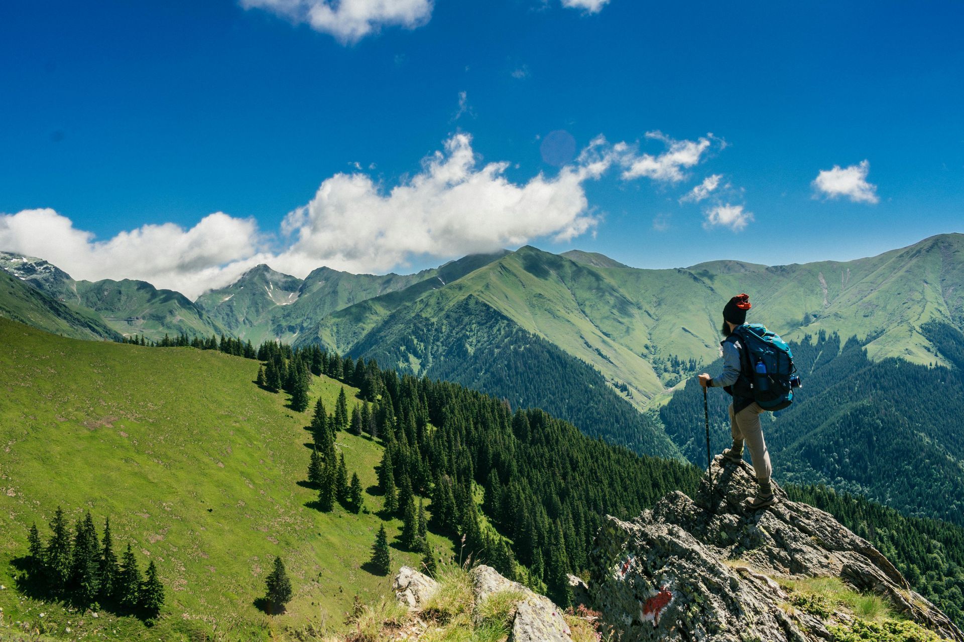 Hiker on a mountain ridge, looking at a green valley and blue sky.