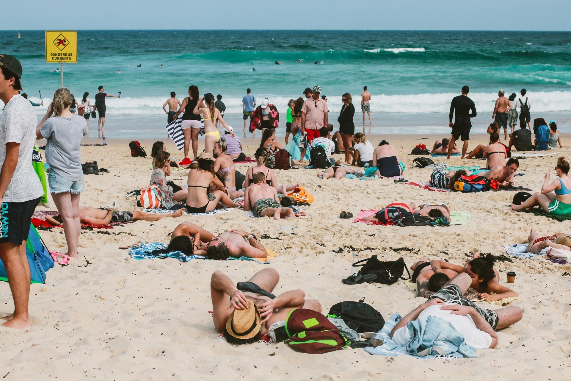 People sunbathing and swimming at a crowded beach on a sunny day.