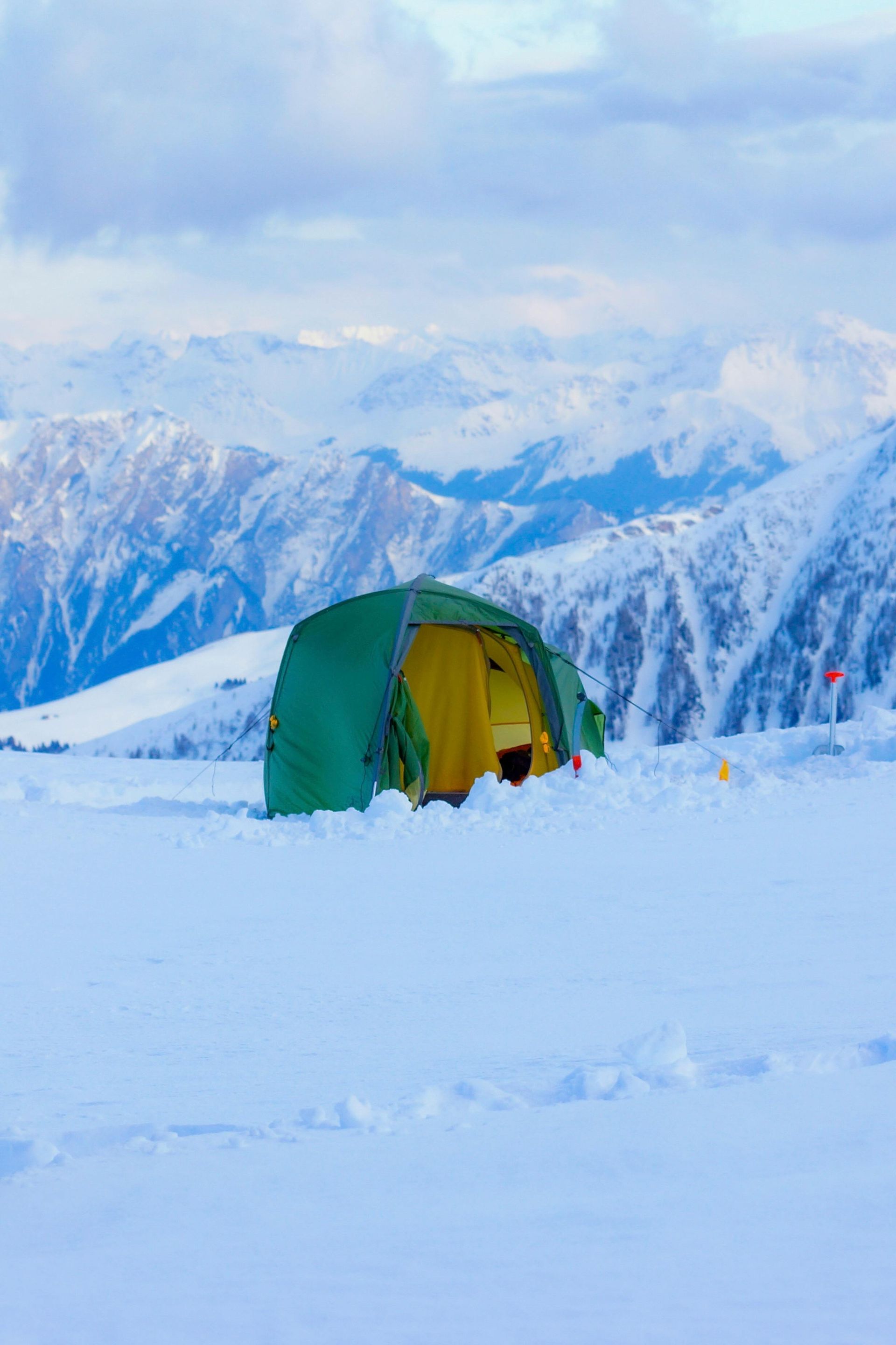 Green tent in snow, mountains in background, likely for camping.