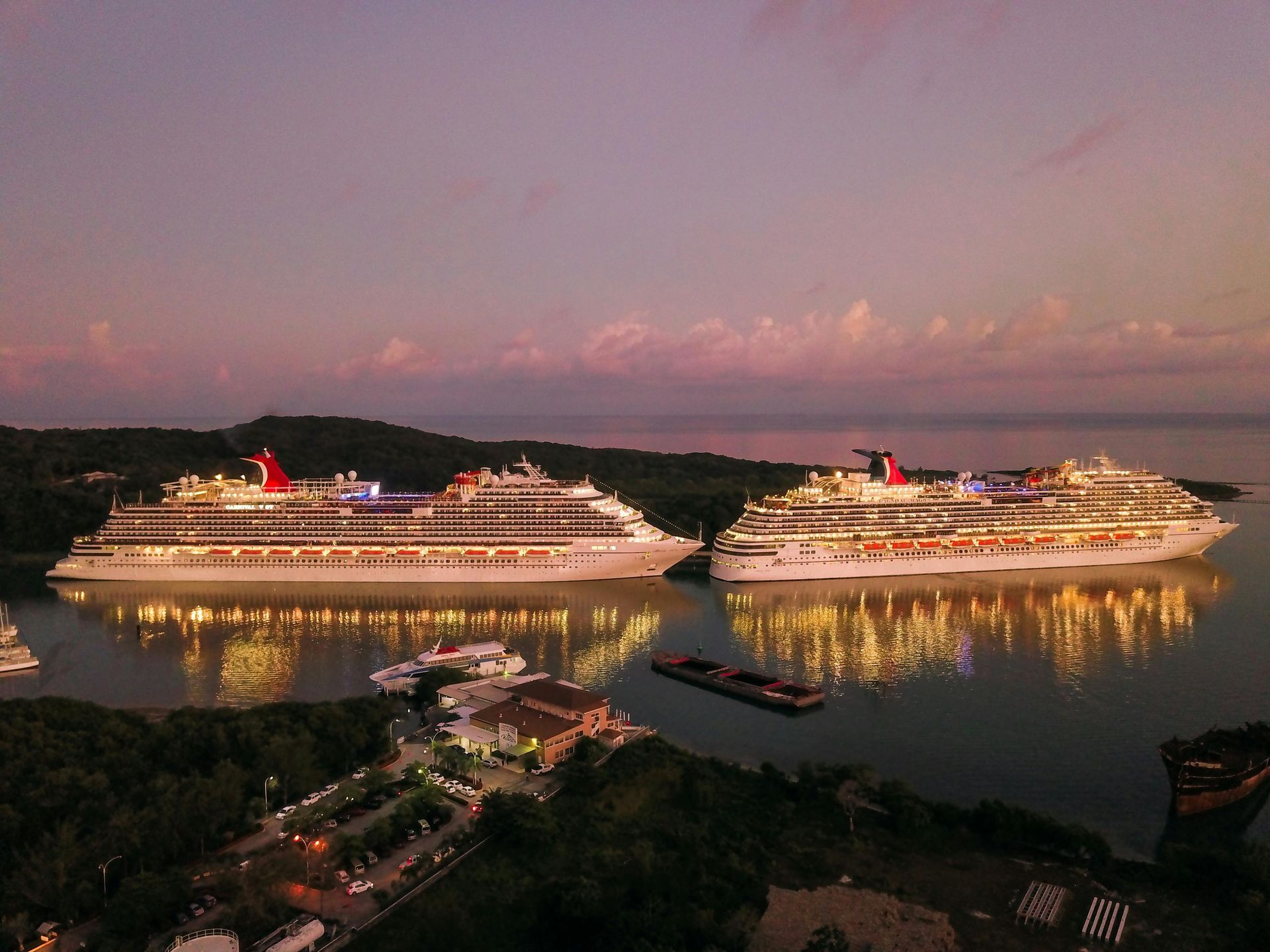 Two illuminated cruise ships in a bay at dusk, reflecting lights on the water.
