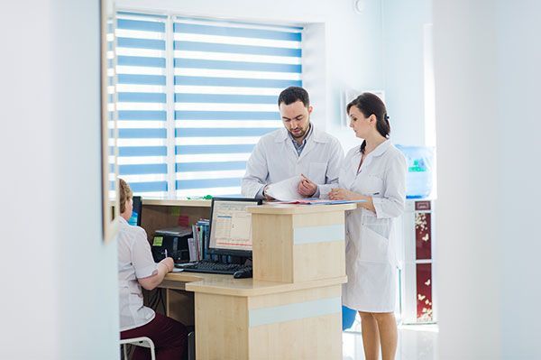 Medical professionals review paperwork at a reception desk in a brightly lit office.