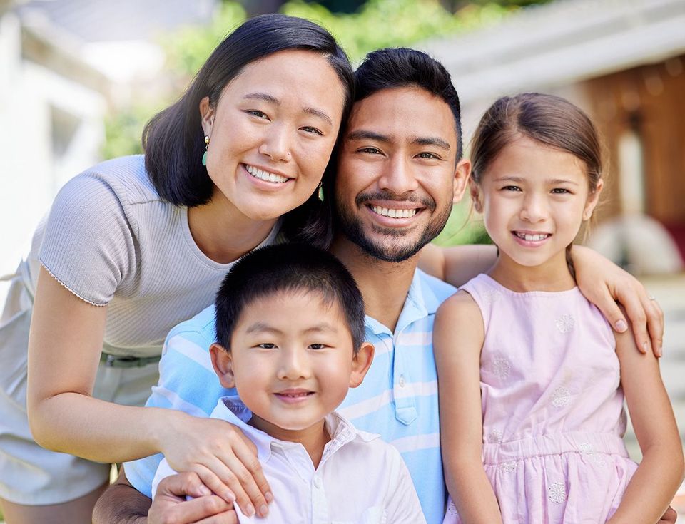 Family of four smiling, posing outdoors. Mother, father, son, and daughter smiling.