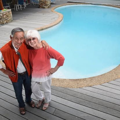 Smiling couple standing by a pool, with the man’s arm around the woman in red and white clothing.