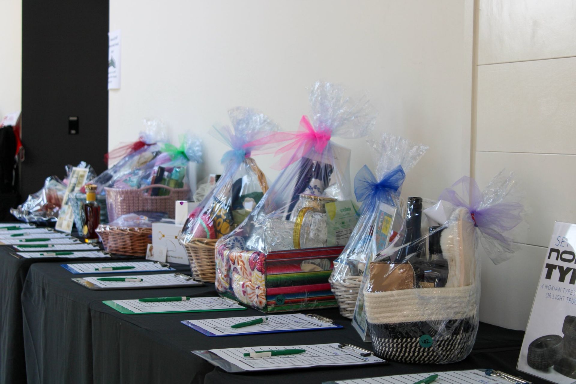 Gift baskets wrapped in clear cellophane line a table against a plain wall.