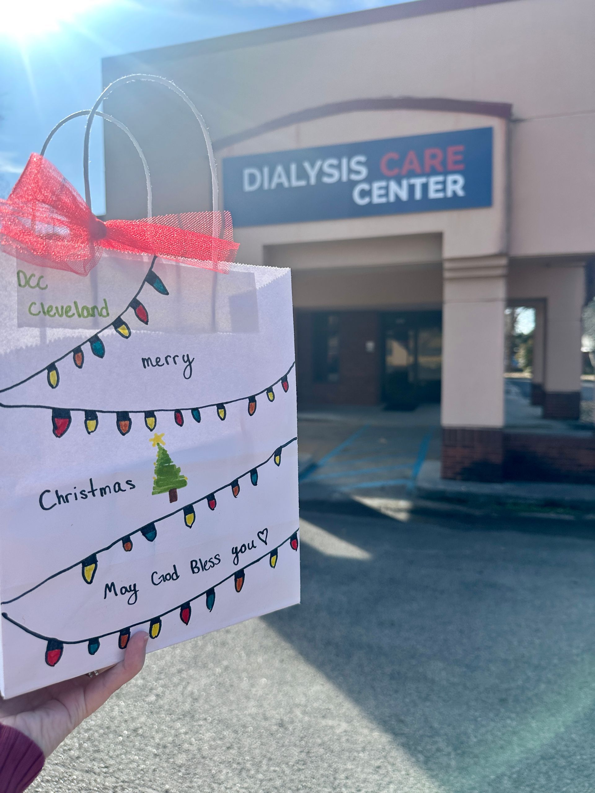 Handmade card held up outside Dialysis Care Center building in bright sunlight.