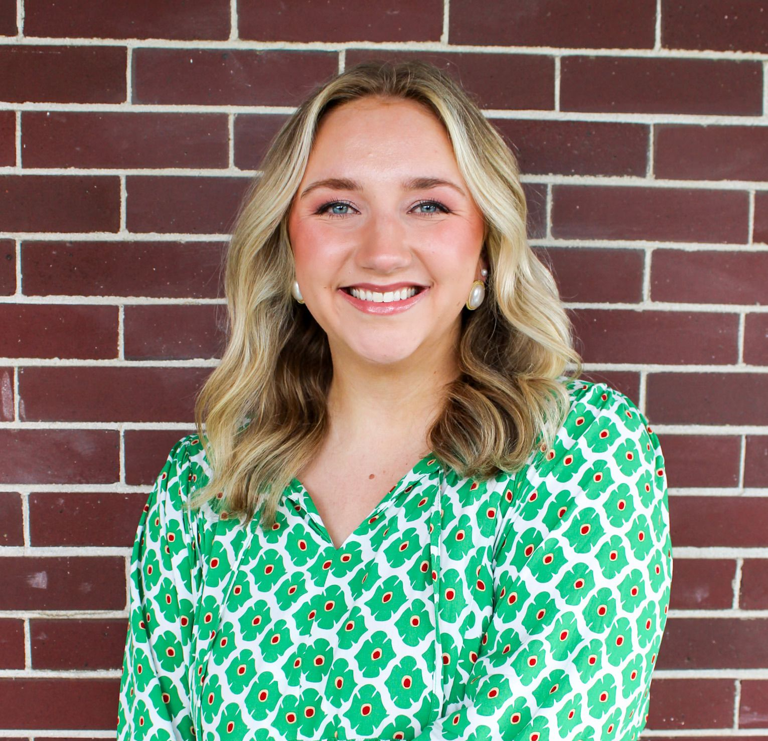 Smiling woman in a green patterned blouse standing in front of a brick wall
