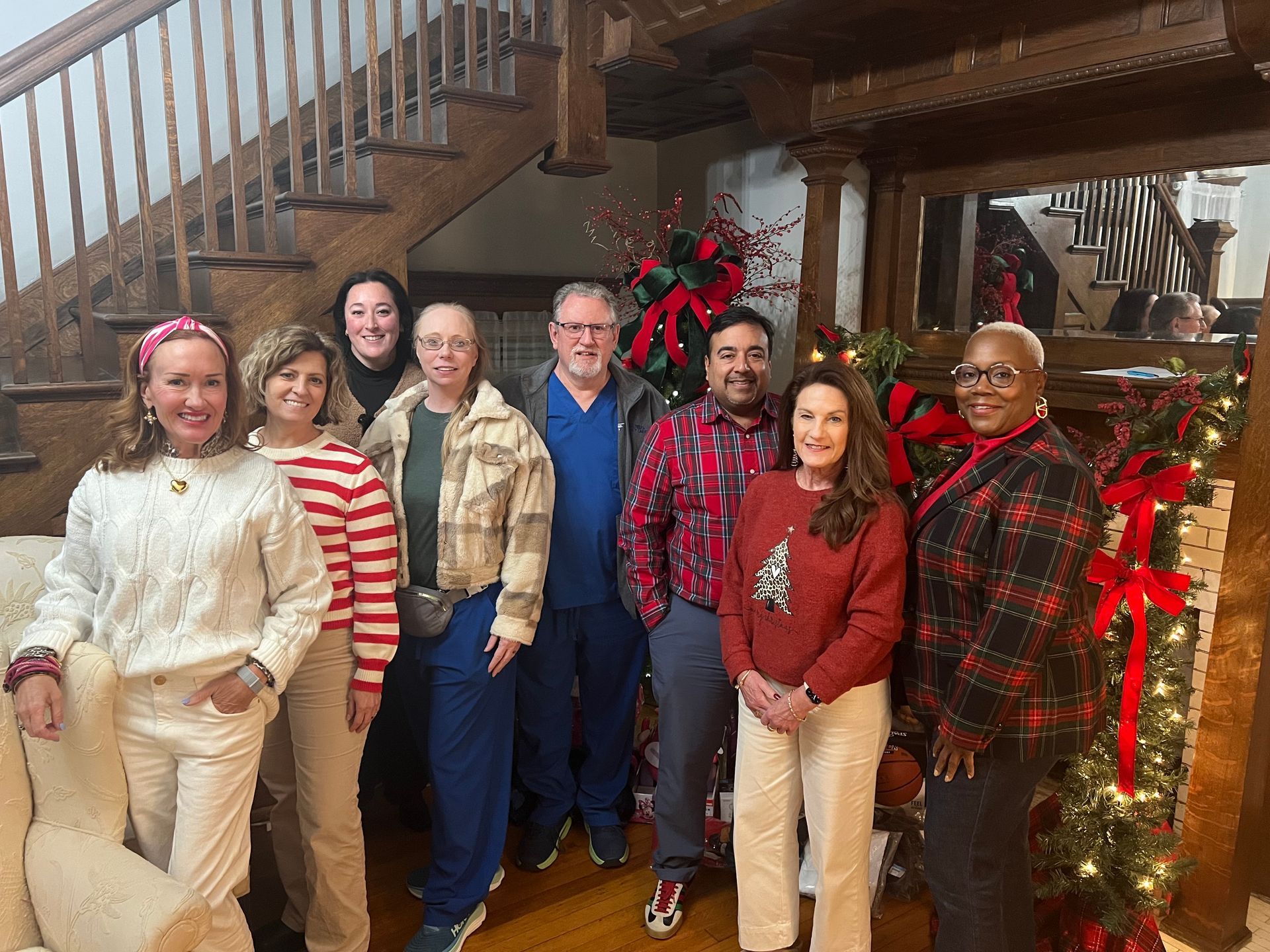 A group of eight people posing on a wooden staircase decorated with red holiday bows and lights.