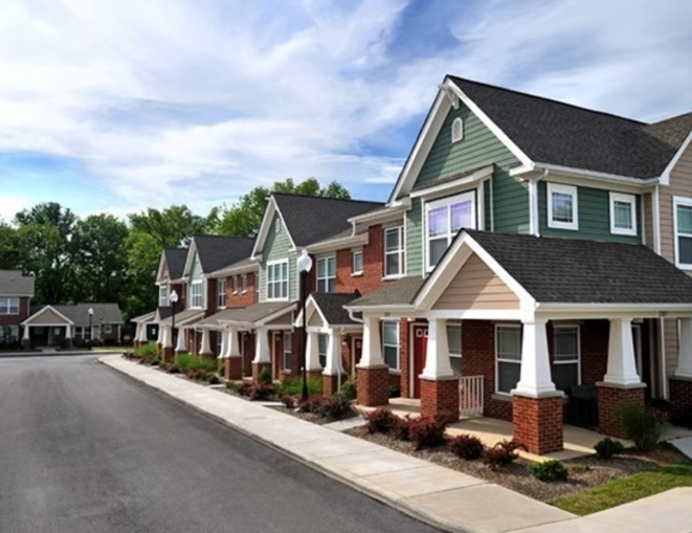 Row of colorful suburban townhouses with front porches along a quiet street under a blue sky