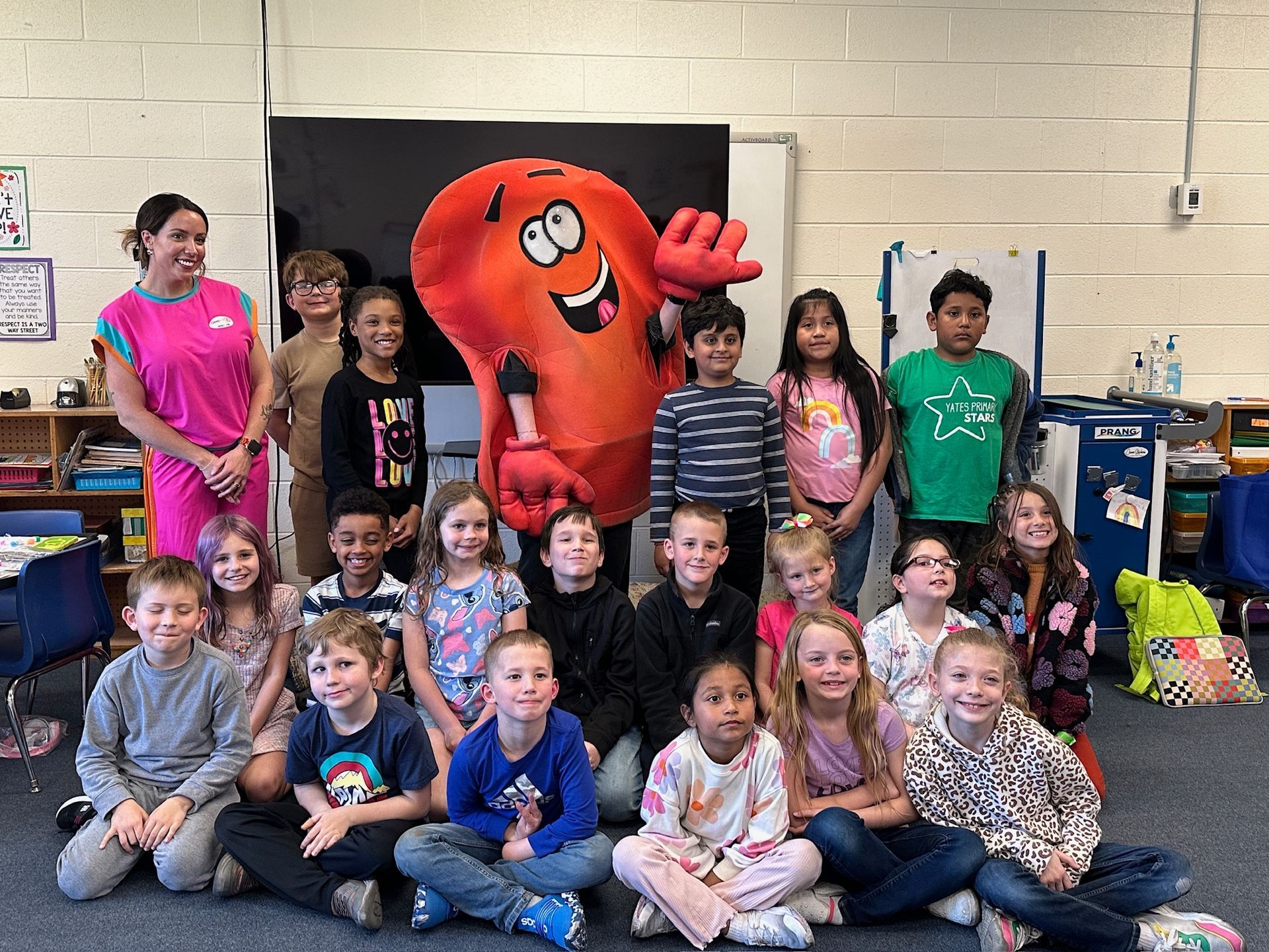 Group of children with a red mascot posing in a classroom, smiling for a photo.